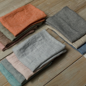 May include: A set of 10 linen kitchen towels in various colors, including orange, gray, blue, green, and pink. The towels are folded and stacked on a wooden surface.