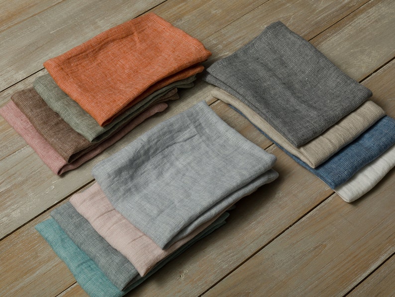 May include: A set of 10 linen kitchen towels in various colors, including orange, gray, blue, green, and pink. The towels are folded and stacked on a wooden surface.