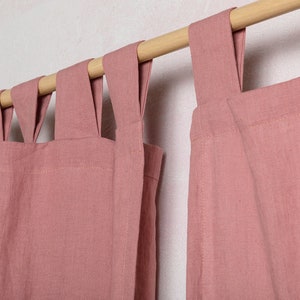 May include: Two dusty rose linen curtains with a wooden rod and a unique looped design at the top.