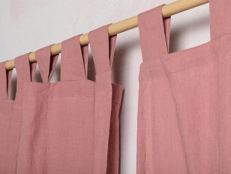 May include: Two dusty rose linen curtains with a wooden rod and a unique looped design at the top.