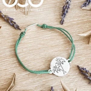 Peut inclure: Bracelet en cordon vert avec un charme en argent représentant un palmier. Le charme est rond et présente un contour détaillé de deux palmiers. Le bracelet est noué et possède un curseur en métal argenté.