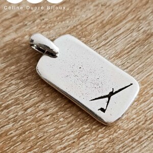 Könnte beinhalten: Rechteckiger Silberanhänger mit kleiner Schlaufe oben. Der Anhänger hat eine schwarze Grafik einer Person, die ein Boot rudert. Der Text "Céline Dupré Bijoux" befindet sich oben.