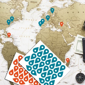 Könnte beinhalten: Eine Weltkarte mit roten und blauen Stecknadeln, die Orte markieren. Die Karte ist umgeben von Reisezubehör, darunter ein Kompass, eine Lupe, ein Fernglas und ein Reisepass. Zwei Blätter mit Aufklebern mit roten und blauen Standort-Symbolen befinden sich im Vordergrund.
