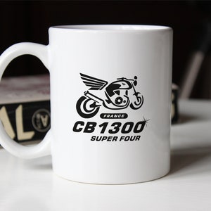 Puede incluir: Taza de cerámica blanca con un gráfico en blanco y negro de una motocicleta con alas. El texto "FRANCE CB1300 SUPER FOUR" está impreso debajo de la motocicleta.