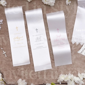 May include: Five white satin ribbons featuring printed text and cross icons. Three ribbons are personalised with names and dates, while two ribbons display the text Lace trim and Tassels, with one featuring lace edging and the other featuring fringe.