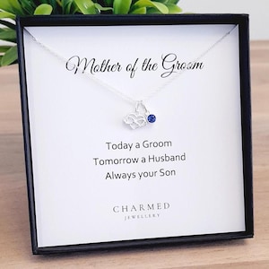 Puede incluir: Un collar de plata en una caja negra con un colgante de piedra azul. La caja tiene una tarjeta blanca con el texto "Madre del novio" y "Hoy un novio Mañana un marido Siempre tu hijo". La tarjeta también tiene el texto "CHARMED JEWELLERY".