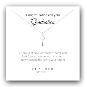 Op de afbeelding: Een zilveren sleutelhangerketting op een witte kaart. De kaart leest "Gefeliciteerd met je afstuderen" en "Nu heb je de sleutel tot je toekomst!" De ketting is van Charmed Jewellery.