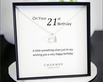 Op de afbeelding: Een zilveren ketting met hartvormige hanger in een zwarte geschenkdoos. De witte inleg bevat de tekst: On Your 21st Birthday, A little something silver just to say wishing you a very happy birthday, en de merknaam CHARMED JEWELLERY.