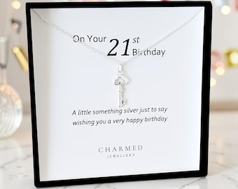 Puede incluir: Un collar con colgante de llave plateada sobre una tarjeta blanca con el texto "On Your 21st Birthday". La tarjeta también dice "A little something silver just to say wishing you a very happy birthday". El collar se muestra en un marco negro.