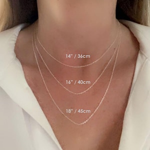 May include: Three silver chains of different lengths, 14 inches, 16 inches, and 18 inches, are shown on a model's neck. The lengths are labeled in inches and centimeters.
