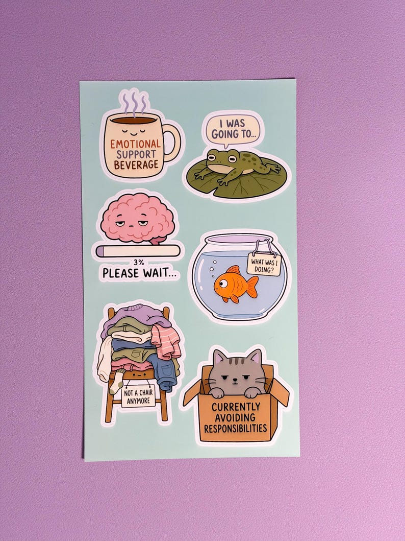 May include: A light blue sticker sheet featuring six illustrations: a coffee mug labelled "Emotional Support Beverage," a frog on a lily pad, a brain with a "3% Please Wait" loading bar, a goldfish in a bowl, a chair piled with clothes, and a cat in a box.