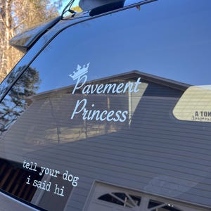 Puede incluir: Un coche negro con una pegatina blanca en la ventana trasera. La pegatina dice "Pavement Princess" con una corona sobre el texto. Debajo de la pegatina hay otra pegatina que dice "tell your dog I said hi".