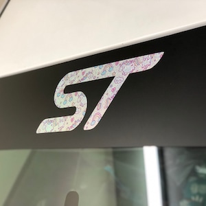 May include: A black and white "ST" logo with a holographic finish featuring a unicorn and rainbow pattern.