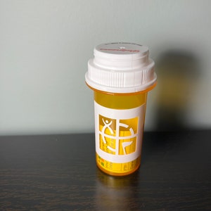 May include: A yellow plastic pill bottle with a white lid and a white label with a graphic of a person and a compass. The label also has the text "You may take one or two pills at a time."