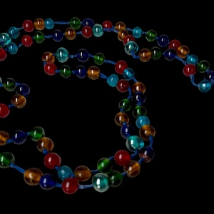 May include: A selection of colourful beaded necklaces. The round beads are in various colours, including red, blue, green, and amber. The beads are strung on a blue cord, creating a vibrant and eye-catching accessory.