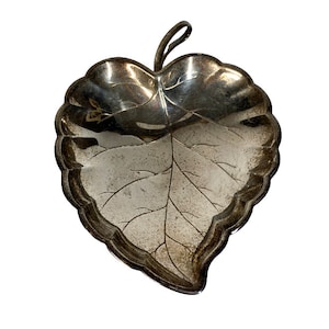 May include: Silver leaf-shaped dish with a detailed vein pattern. The dish is made of metal and has a shiny finish.