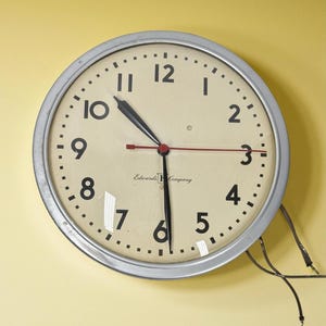 Può includere: Un orologio rotondo vintage con una cornice in metallo color argento. Il quadrante color crema presenta numeri e lancette neri, con una lancetta dei secondi rossa. L'ora visualizzata è circa le 10:16. Il testo "Edwards & Company" è stampato sul quadrante.