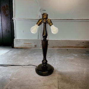 May include: A dark wood floor lamp with a black base and two light bulbs. The lamp has a brass socket and a chain hanging from the top.
