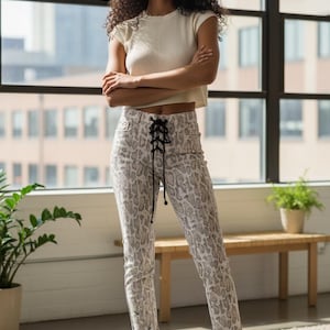 Peut inclure: Une femme porte un haut court crème et un pantalon à imprimé serpent avec un détail de laçage noir. Le pantalon est blanc et gris. Elle porte des baskets blanches.