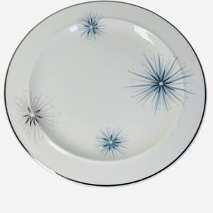 Peut inclure: Assiette en céramique blanche avec un bord noir et des motifs d'éclats d'étoiles bleues. L'assiette a un centre légèrement creux et est probablement destinée à servir des aliments. Les éclats d'étoiles sont de tailles variables.