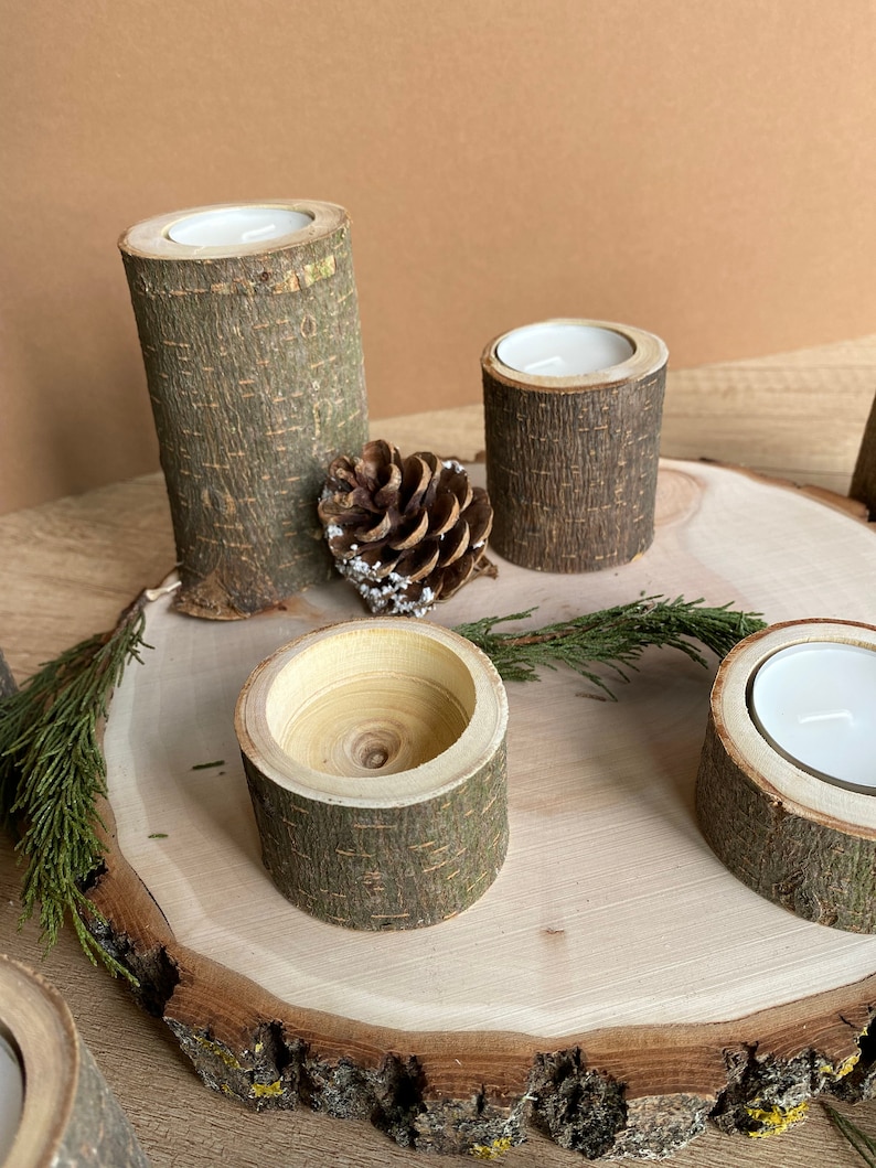 May include: A wooden candle holder set with four individual holders, each made from a tree branch with the bark still on. The holders are arranged on a wooden slice with a pine cone in the center.