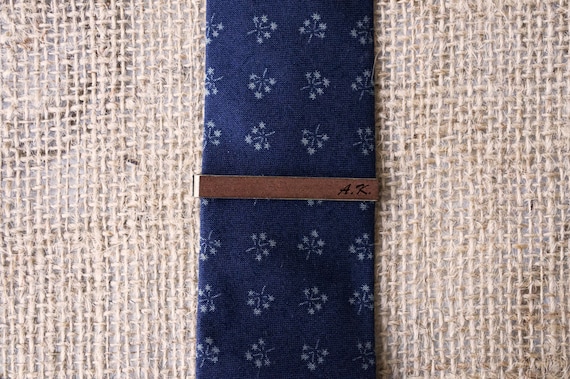 Dark wood tie clips with custom engraving are a genuinely sharp alternative to boring metal bars — the natural grain makes each one subtly unique.