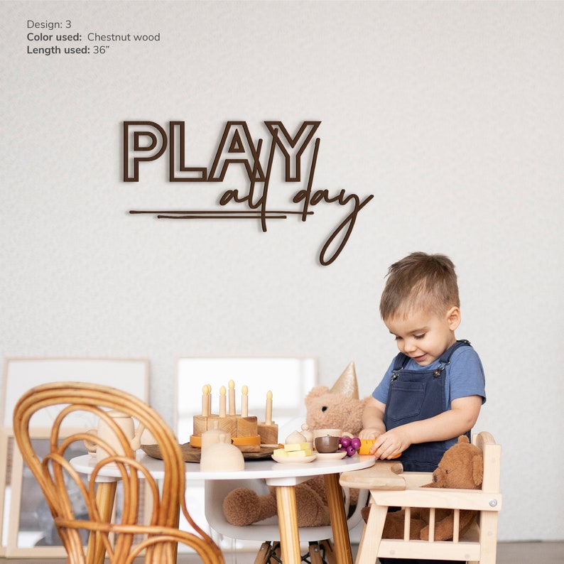 May include: A wooden sign with the text "PLAY all day" in brown lettering. A young child is playing with toys at a table in front of the sign.