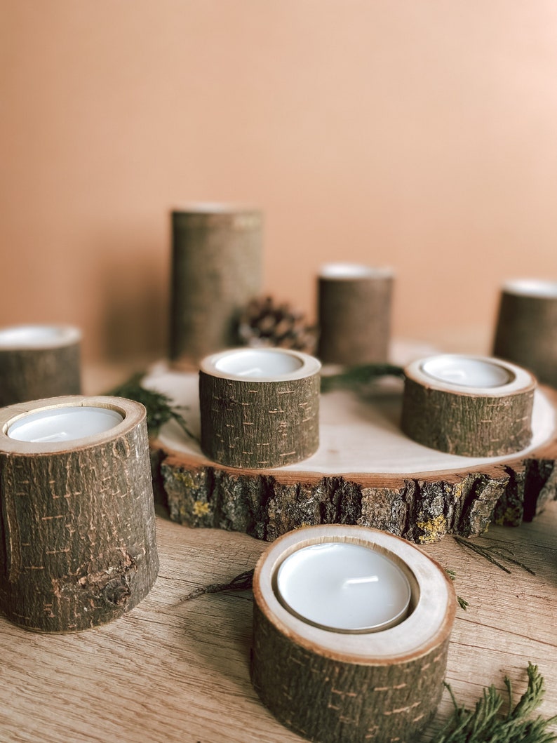 May include: A set of six wooden candle holders, each with a natural bark finish, arranged on a wooden slice. The candle holders are perfect for tea lights or votive candles.