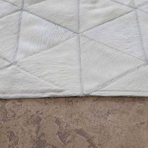 White Triangles Patchwork Cowhide Rug on stone floor. The Kata cowhide area rug in cream, off-white hide. Available in custom and standard siezes 8x10ft, 9x12ft, 10x13ft. Free shipping to USA and Canada