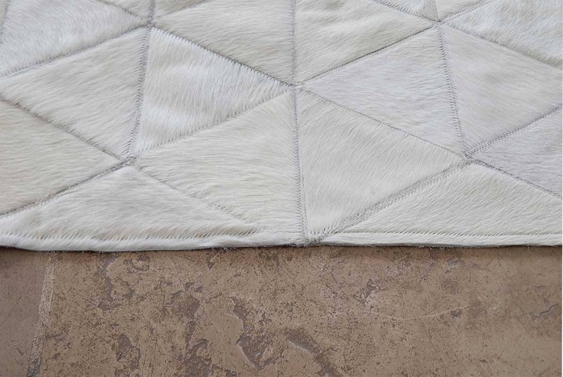 White Triangles Patchwork Cowhide Rug on stone floor. The Kata cowhide area rug in cream, off-white hide. Available in custom and standard siezes 8x10ft, 9x12ft, 10x13ft. Free shipping to USA and Canada