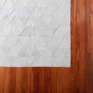Classic wood floor with White Triangles Patchwork Cowhide Rug. The Kata cowhide area rug in cream, off-white hide. Available in custom and standard siezes 8x10ft, 9x12ft, 10x13ft. Free shipping to USA and Canada