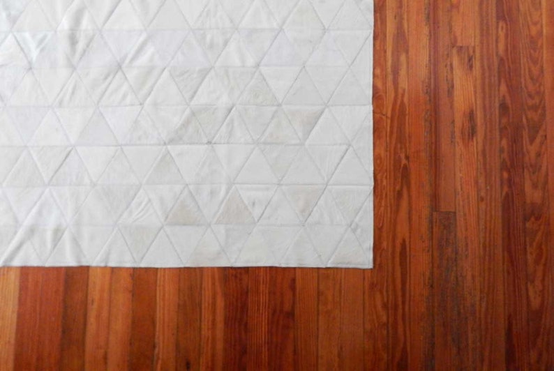 Classic wood floor with White Triangles Patchwork Cowhide Rug. The Kata cowhide area rug in cream, off-white hide. Available in custom and standard siezes 8x10ft, 9x12ft, 10x13ft. Free shipping to USA and Canada
