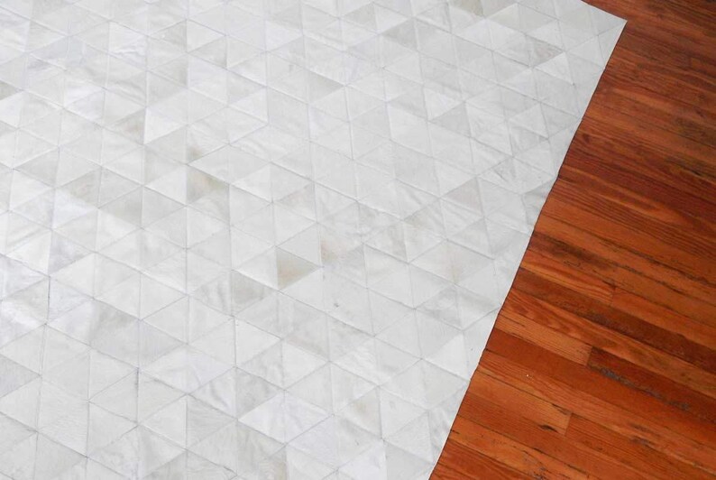 White Triangles Patchwork Cowhide Rug on wooden floor. The Kata cowhide area rug in cream, off-white hide. Available in custom and standard siezes 8x10ft, 9x12ft, 10x13ft. Free shipping to USA and Canada