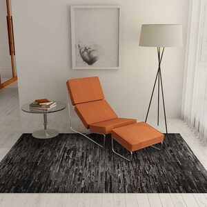 Pu&ograve; includere: Una poltrona e un pouf arancioni con struttura cromata poggiano su un tappeto grigio scuro e nero. Un tavolino rotondo in vetro con libri e una lampada da terra con paralume bianco sono anch'essi nella stanza. Una foto incorniciata &egrave; appesa al muro.