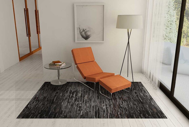 Pu&ograve; includere: Una poltrona e un pouf arancioni con struttura cromata poggiano su un tappeto grigio scuro e nero. Un tavolino rotondo in vetro con libri e una lampada da terra con paralume bianco sono anch'essi nella stanza. Una foto incorniciata &egrave; appesa al muro.