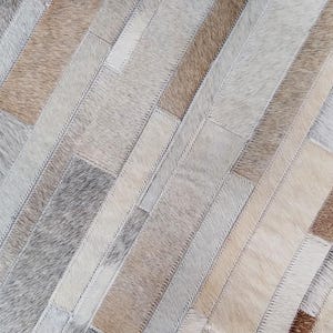 Stitch and texture detail of a taupe cowhide rug in striped patches. Warm natural tones and soft feel.