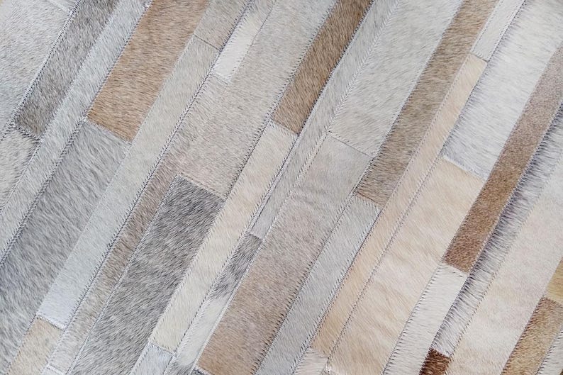 Stitch and texture detail of a taupe cowhide rug in striped patches. Warm natural tones and soft feel.