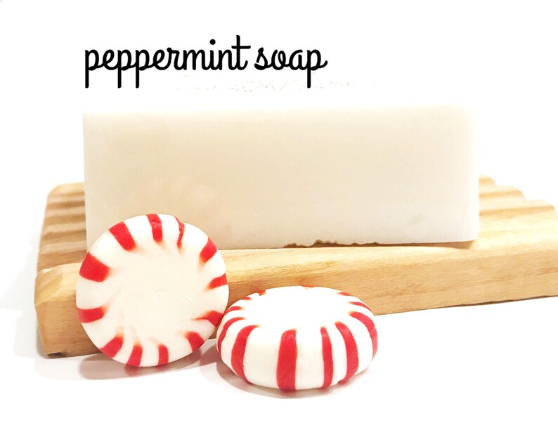 May include: A bar of white peppermint soap rests on a wooden soap dish, accompanied by two peppermint candies with red and white stripes. The text "peppermint soap" is written in black cursive above the soap.