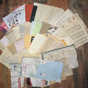 Puede incluir: Una colección de papel efímero variado dispuesto en forma de abanico, que incluye páginas de libros antiguos, partituras musicales, cartulina con patrones coloridos, papel rayado, mapas impresos y varios recortes texturizados en tonos neutros.