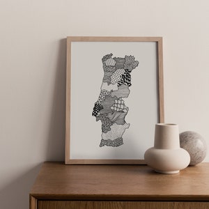 May include: A framed art print featuring a detailed black and white illustration of Portugal. The artwork is filled with various patterns and textures, creating a unique and artistic representation of the country's outline. The print is displayed on a wooden surface.