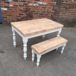 May include: A white painted wooden table with a natural wood top and turned legs. A matching white painted wooden bench with a natural wood top and turned legs is in front of the table.