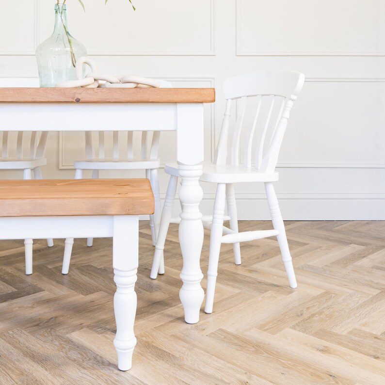 May include: White farmhouse style dining table with a natural wood top and turned legs. The table is paired with a matching bench and chairs.