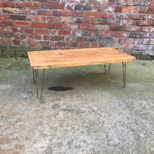 May include: A rustic wooden coffee table with a natural wood finish and hairpin legs. The table is made from reclaimed wood and has a simple, modern design.