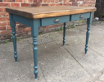 May include: A teal blue desk with two drawers and turned legs. The desk top is made of natural wood.