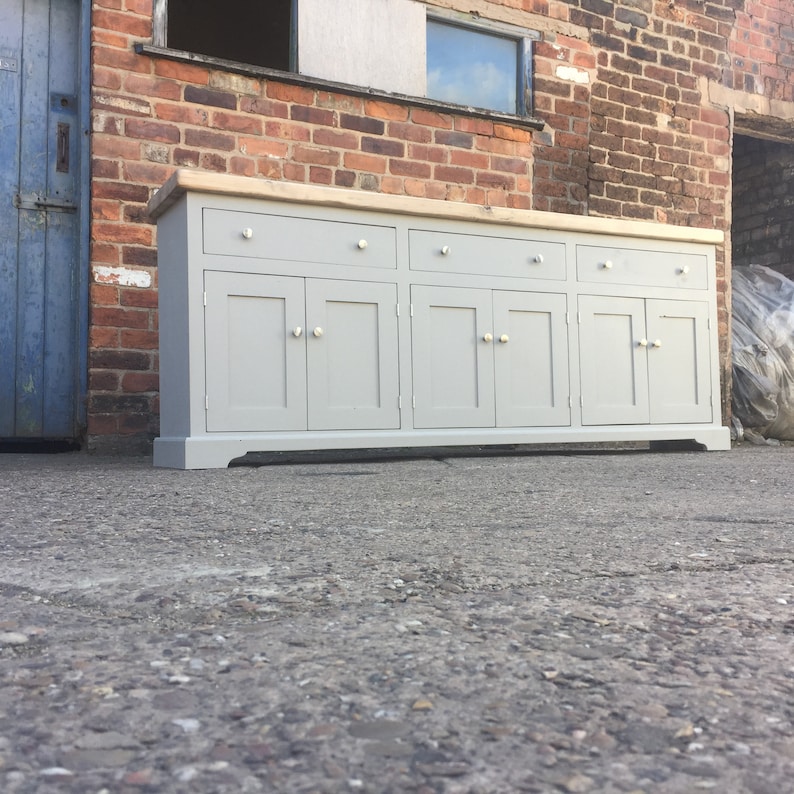 Op de afbeelding: Een grijs houten dressoir met zes deuren en twee laden. De bovenkant van het dressoir is gemaakt van licht hout.