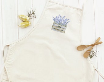 May include: A white cotton apron with a pocket and adjustable straps. The apron has a lavender floral design in a wooden crate.