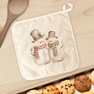 May include: A cream-colored pot holder featuring a watercolor illustration of two snowmen wearing hats and scarves. One snowman has a red and white striped scarf, and the other has a tan scarf. The pot holder has a loop for hanging.