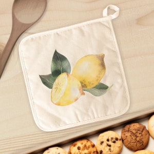 May include: A white cotton pot holder with a watercolor illustration of two lemons and green leaves.