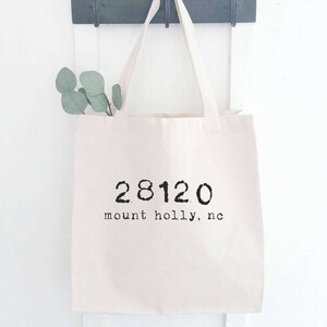 May include: A white canvas tote bag with black text that reads "28120 mount holly, nc".