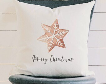 May include: A white throw pillow with a watercolor-style gingerbread star design and the words "Merry Christmas" in black script. The pillow is displayed on a dark gray chair, perfect for holiday decor.